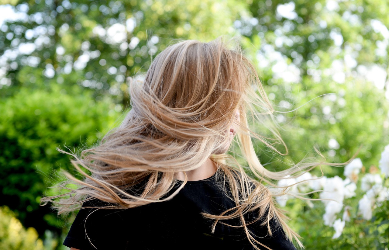 Frau mit langen blonden Haaren im Wind vor grünem Hintergrund